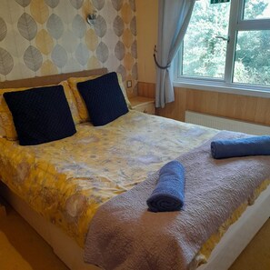 Una cama con una colcha floral, dos almohadas oscuras y toallas enrolladas.