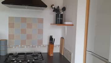 Una cocina con estufa a gas, extractor, salpicadero de azulejos, mueble de madera y refrigerador.