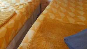 A hotel room with two beds, each with a patterned bedspread and pillows. There is a nightstand with a teddy bear between the beds.
