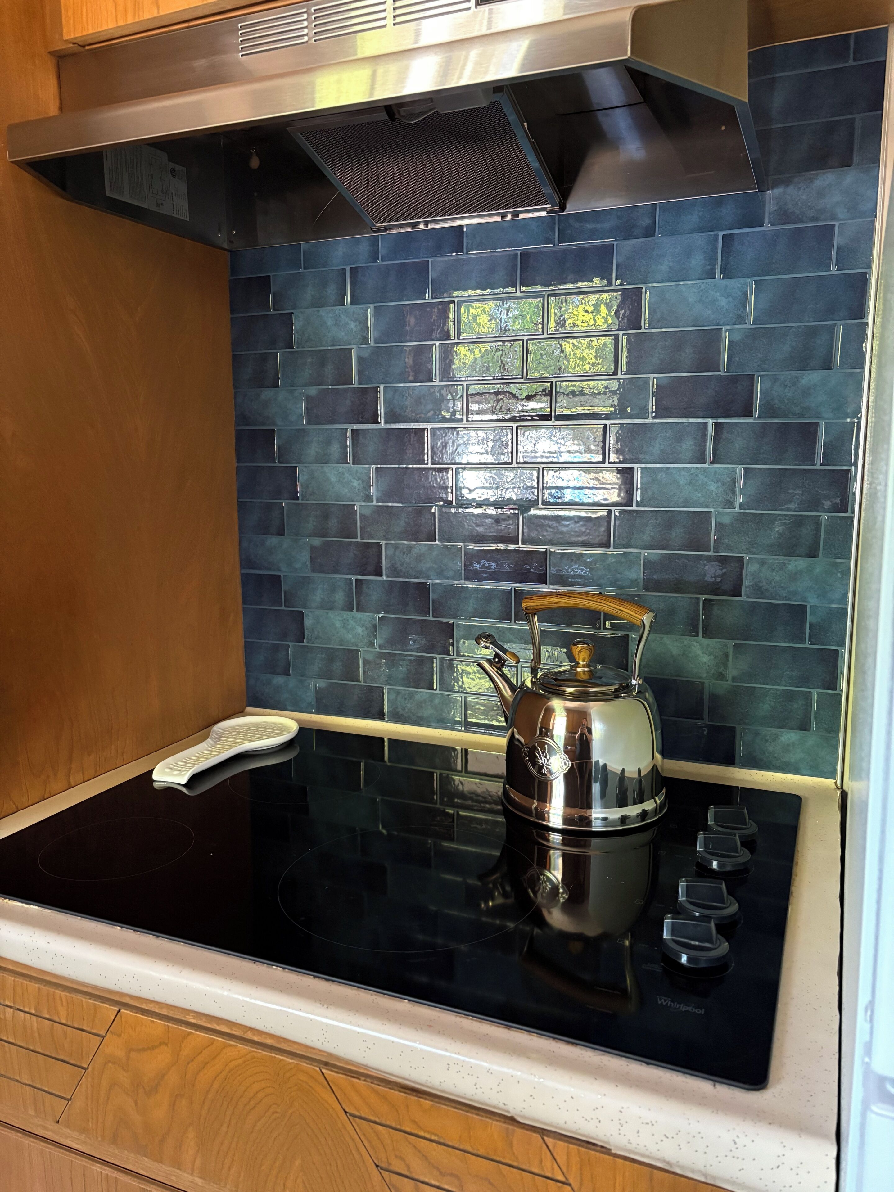 A kitchen with a black stovetop, a stainless steel kettle, and a backsplash with blue tiles.