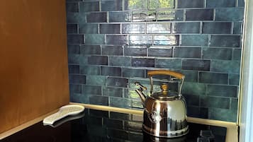 A kitchen with a black stovetop, a stainless steel kettle, and a backsplash with blue tiles.