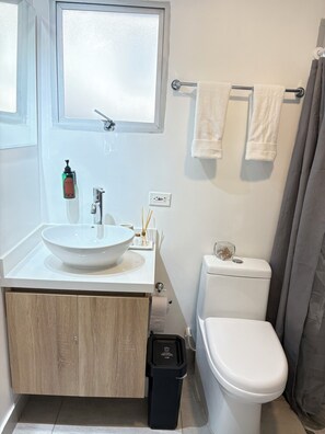 Ein Badezimmer mit einem weißen Waschbecken, einer Toilette, einem Fenster und einem Handtuchhalter.