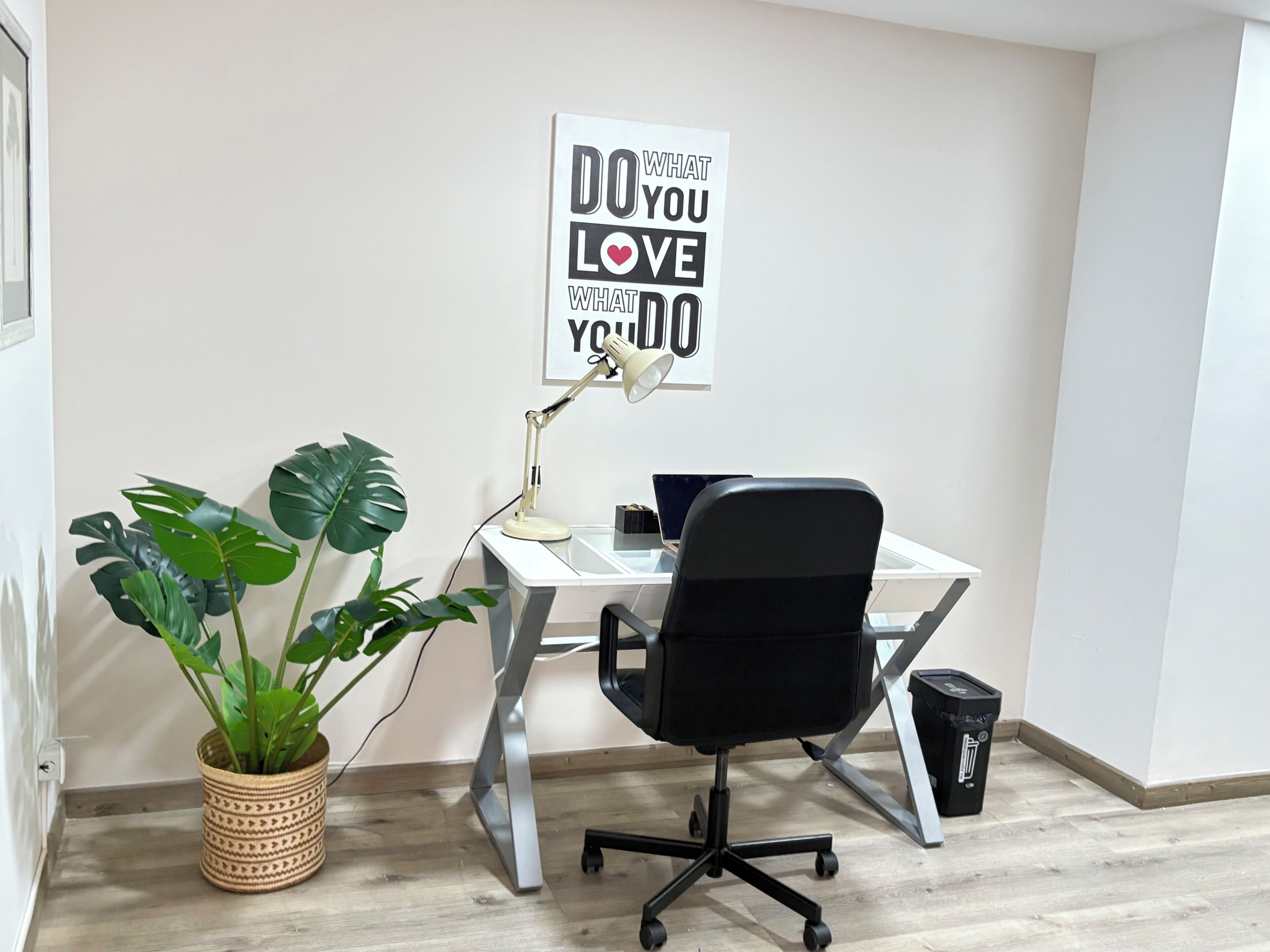 Un espacio de trabajo con un escritorio, una silla, una planta en maceta, una lámpara de escritorio y un cartel motivacional en la pared.