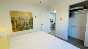 A bedroom with a bed, a painting, a closet, and a door leading to a kitchen. - Comfort, Convenience & Steps from Local Flavors + King Bed! (Long Beach)