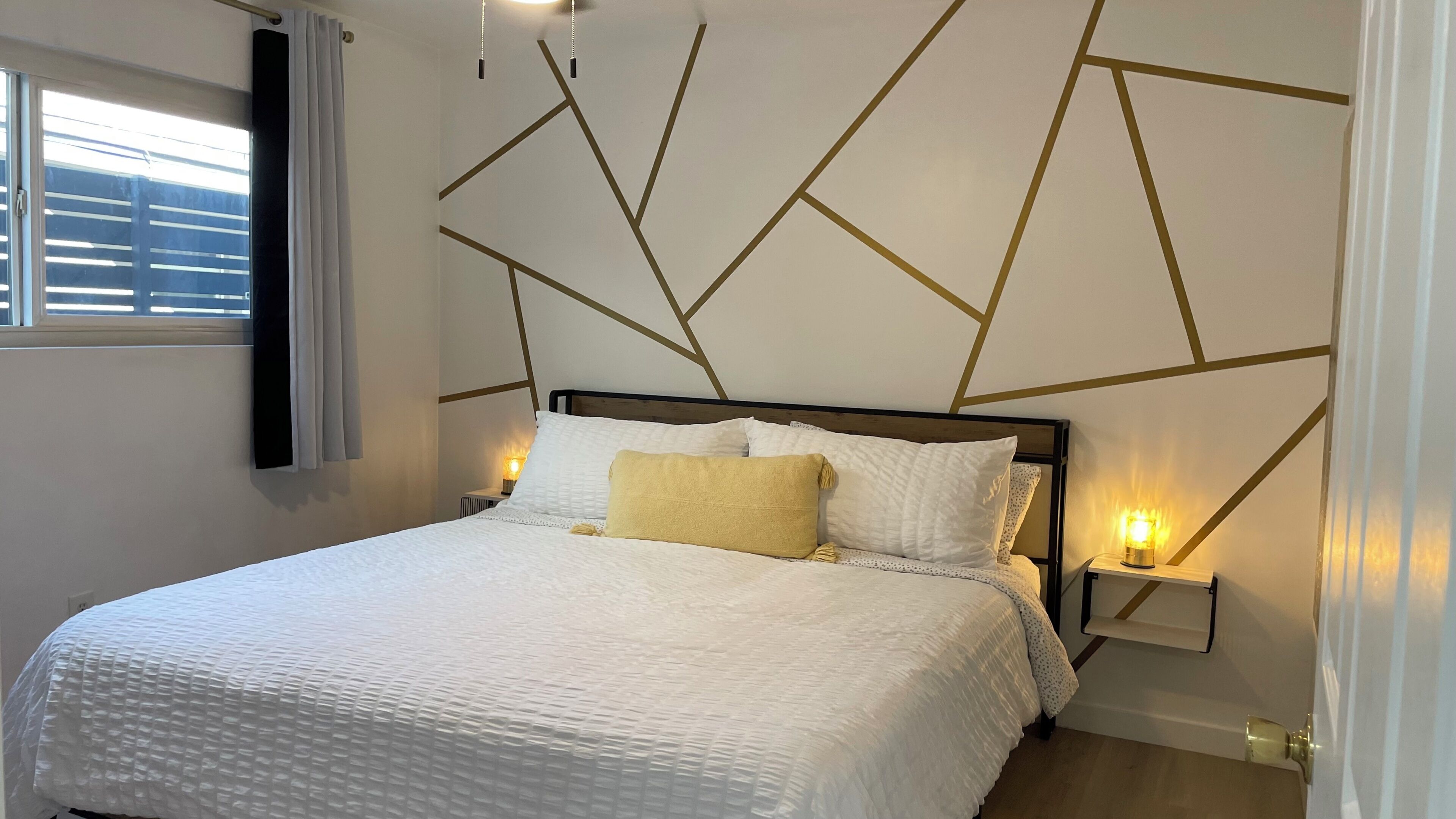 A modern bedroom with a geometric wall design, a white bed with a textured cover, and bedside lamps.