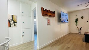 Ein Zimmer mit Holzboden, einer verschließbaren Tür, einem an der Wand befestigten Fernseher und einem gerahmten Bild.