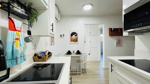 Een moderne keuken met witte kasten, een zwarte kookplaat en een eethoek met tafel en stoelen.