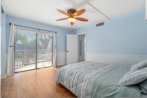 A bedroom with a bed, a ceiling fan, a window with blinds, and a door. - New Smyrna Beachside 2BR 3 Bath Condo Balcony (New Smyrna Beach)