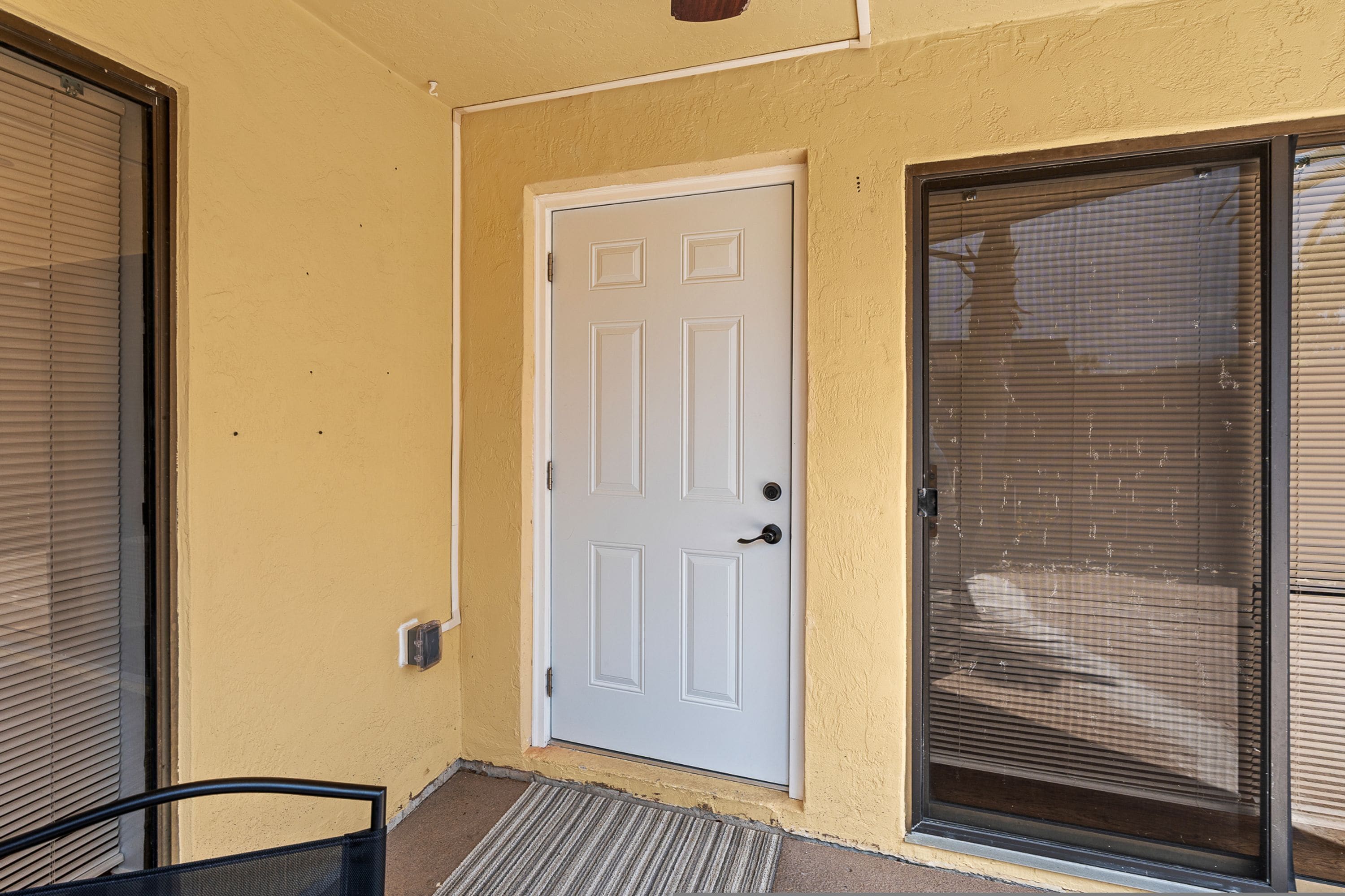 A white door with a small window, a sliding glass door with blinds, and a black chair outside.