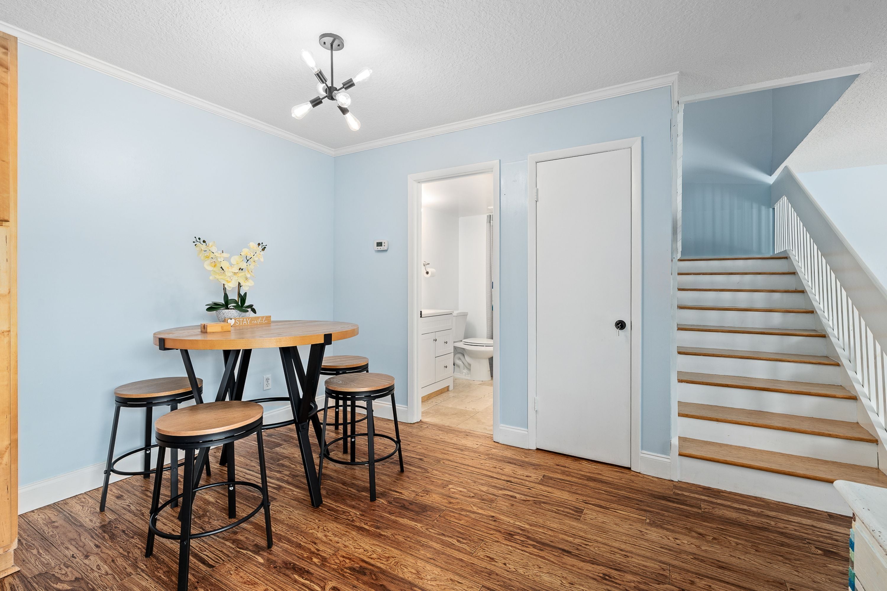 A dining area with a round table and stools, a ceiling fan, and a staircase leading to another room.
