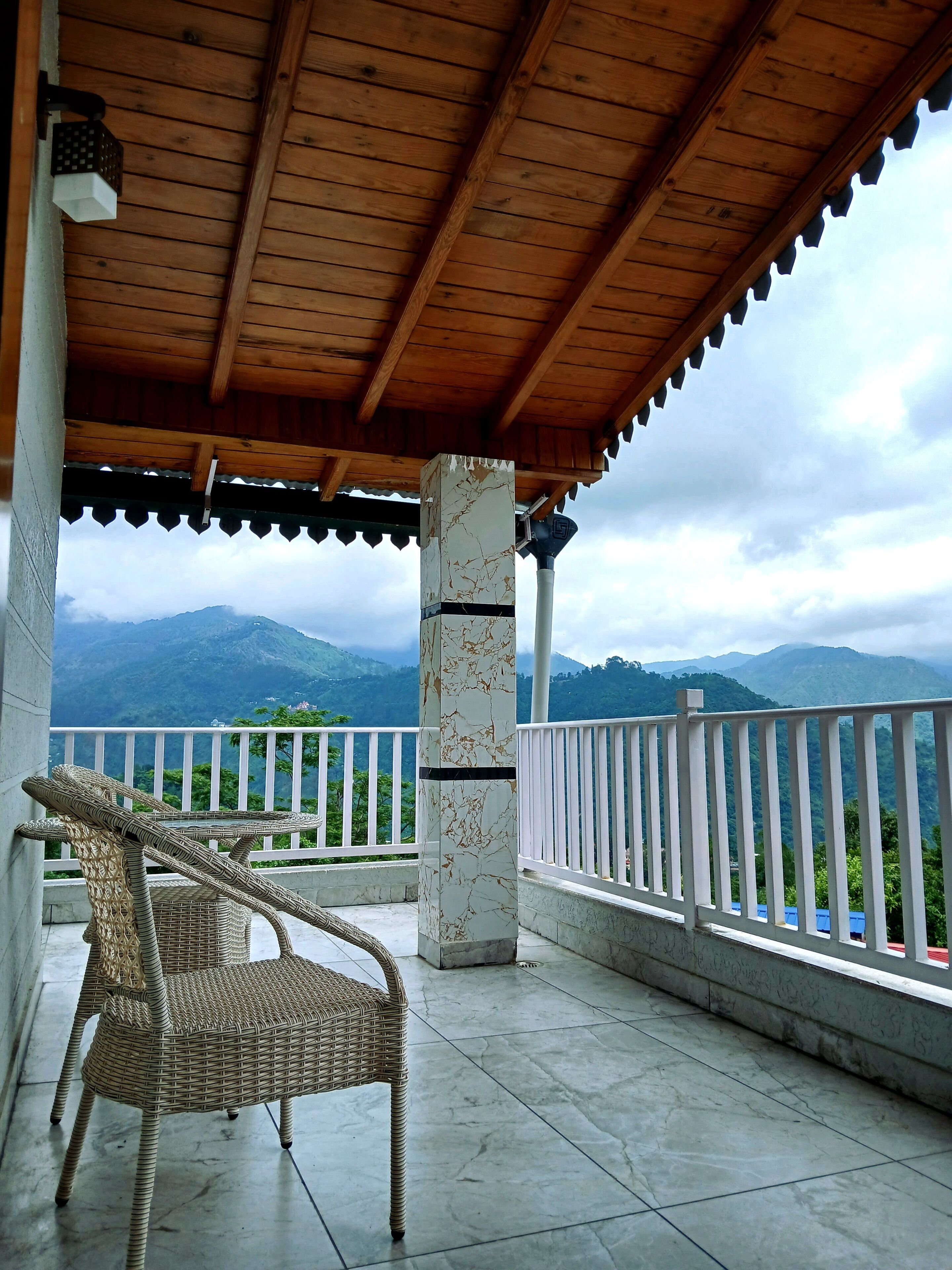 A covered balcony with a wicker chair, white railing, and a view of mountains.