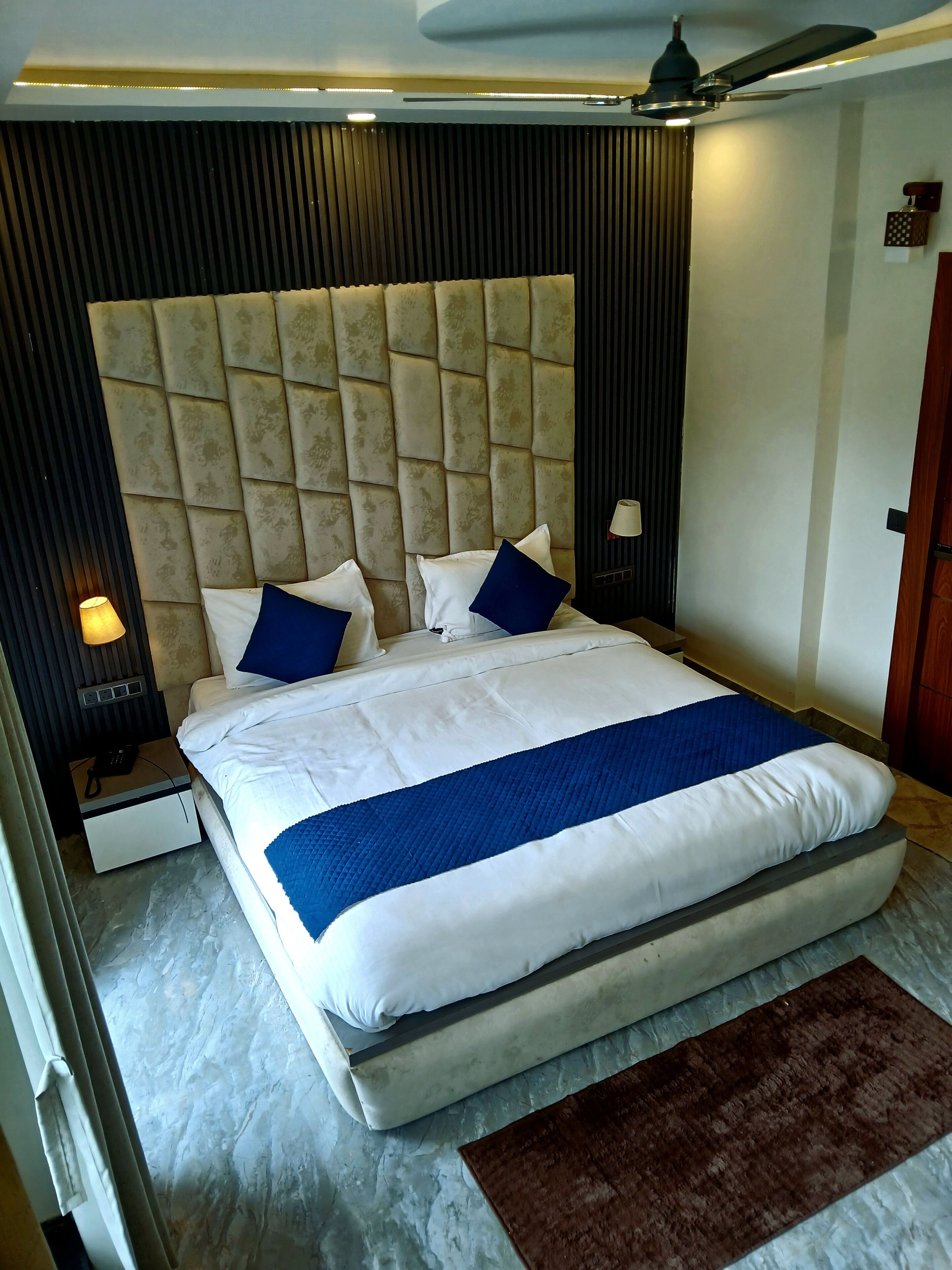 A hotel room with a large bed, a headboard, a nightstand, a lamp, and a ceiling fan.