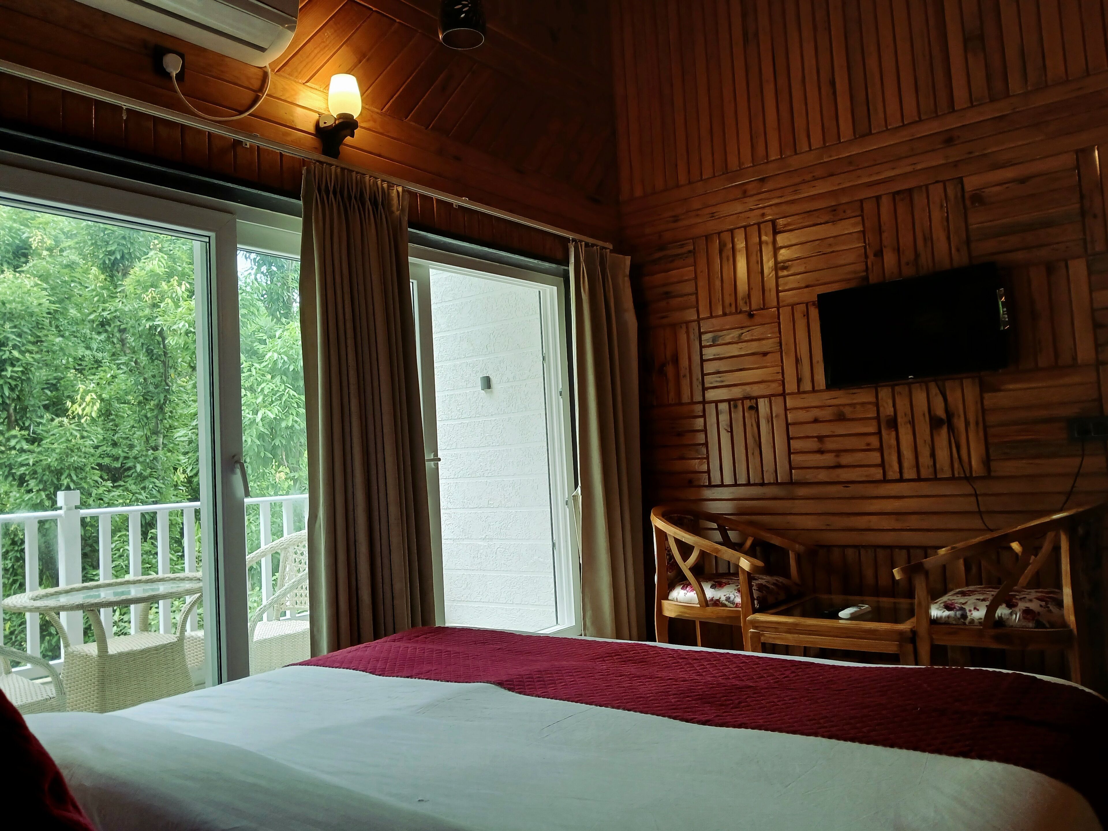 A room with a bed, a television mounted on the wall, a balcony with a railing, and a window with curtains.