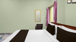 Quarto de hotel com uma cama grande, uma cadeira, janela com cortinas e um espelho na parede.