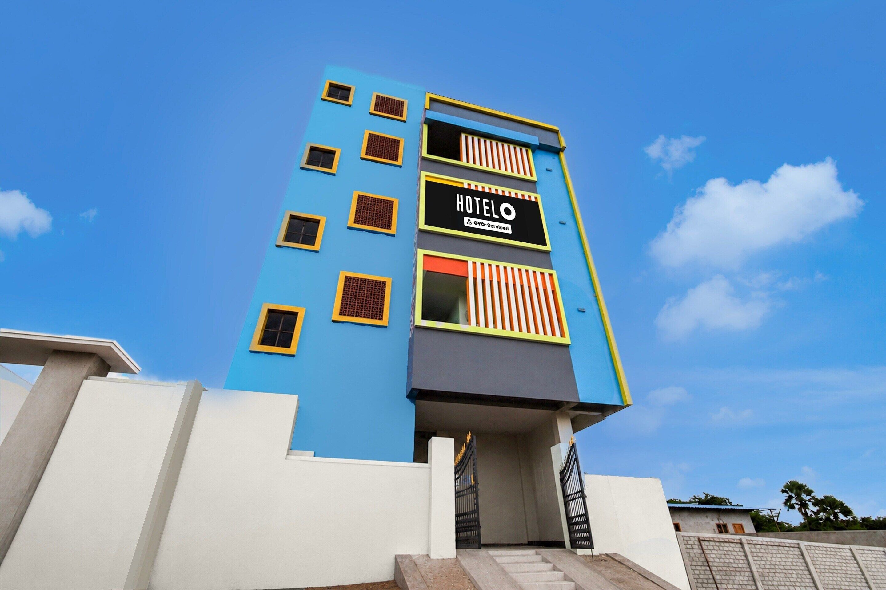 A hotel building with a blue facade, multiple windows, and a sign indicating it is serviced by OYO.