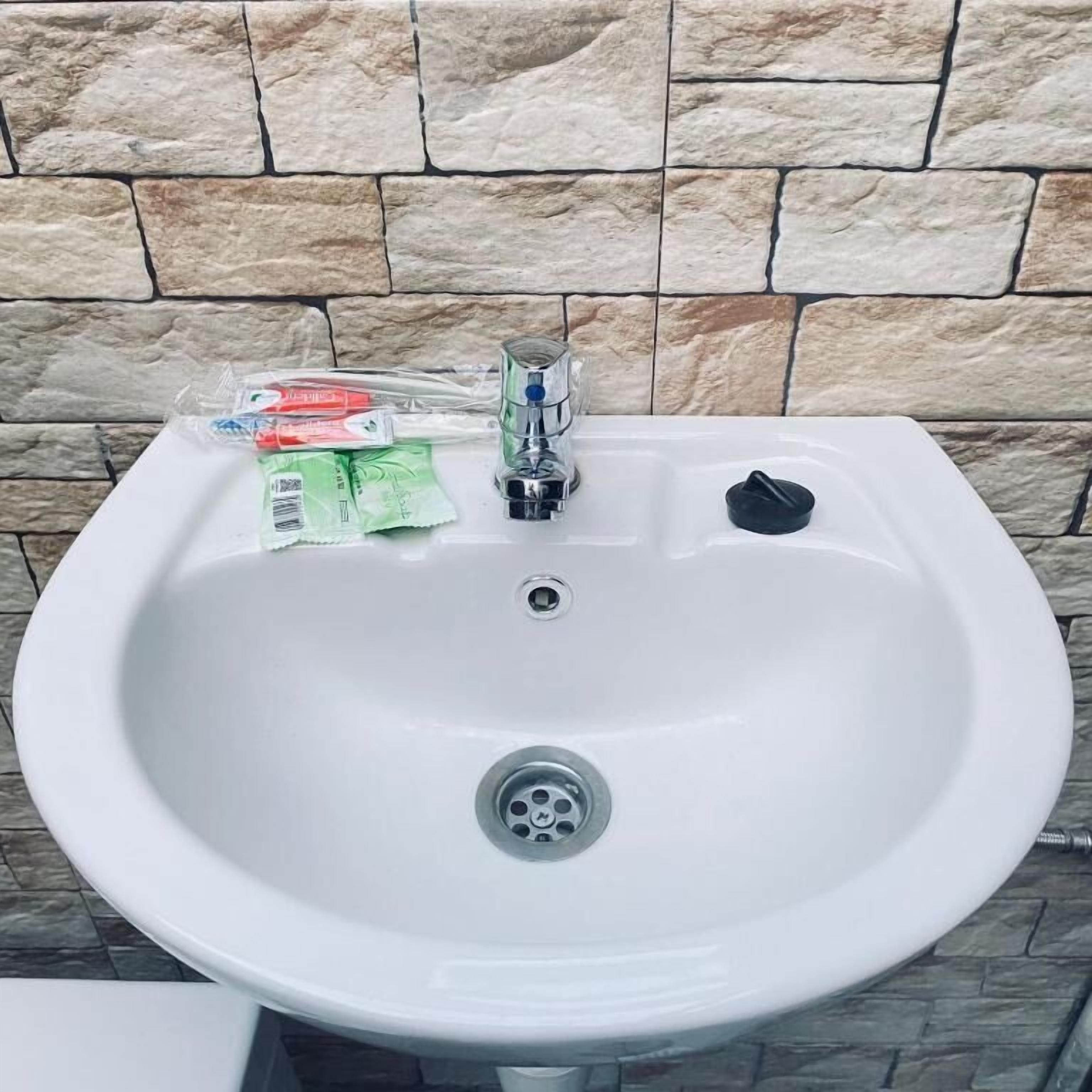 A white sink with a faucet, a drain, and a soap dispenser against a stone wall.