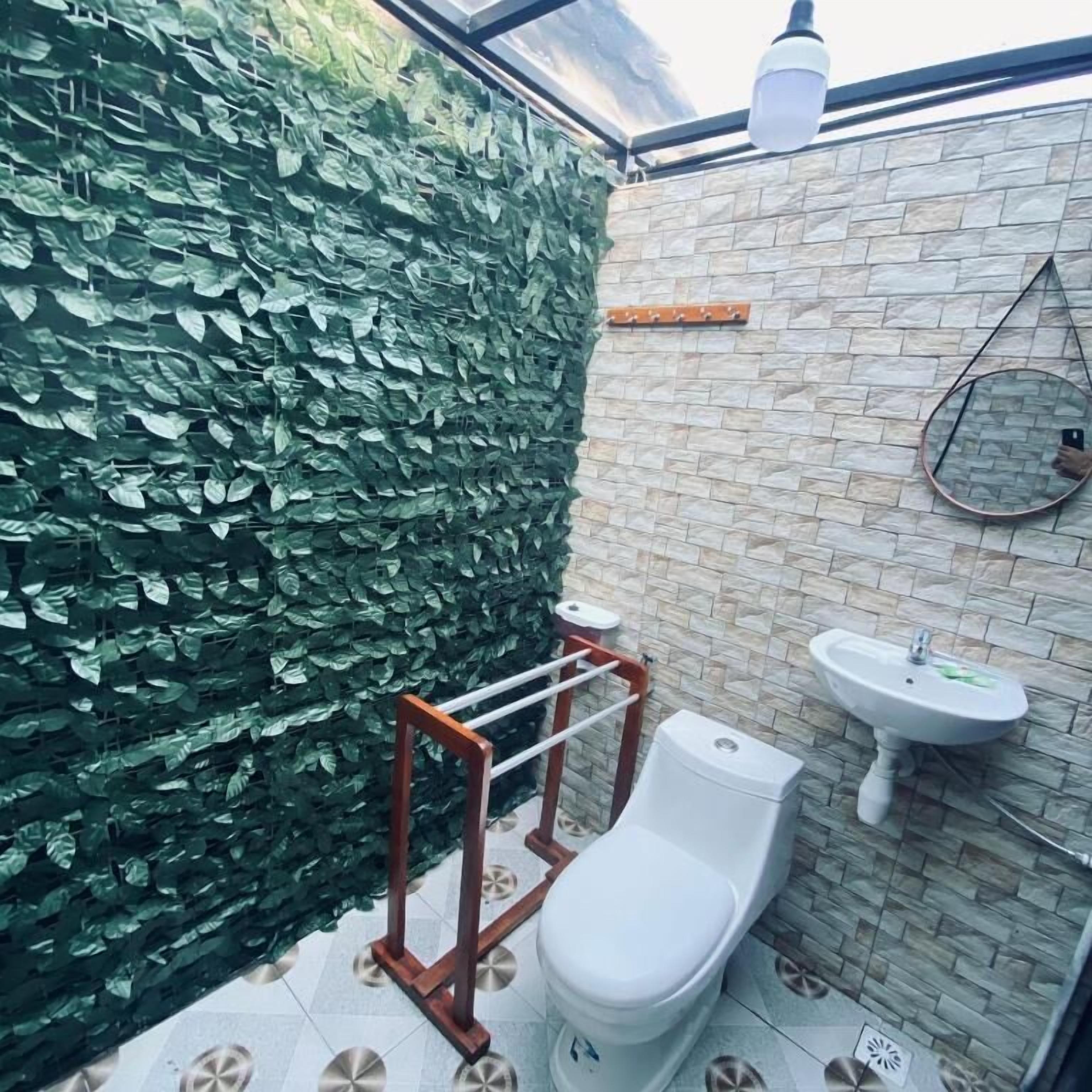 Une salle de bain avec un mur recouvert de feuilles vertes, des toilettes blanches, un porte-serviettes en bois, un lavabo et un miroir.