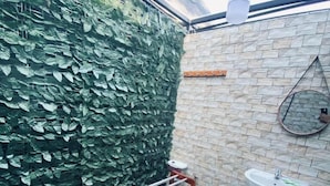 A bathroom with a green leafy wall, a white toilet, a wooden towel rack, a sink, and a mirror.