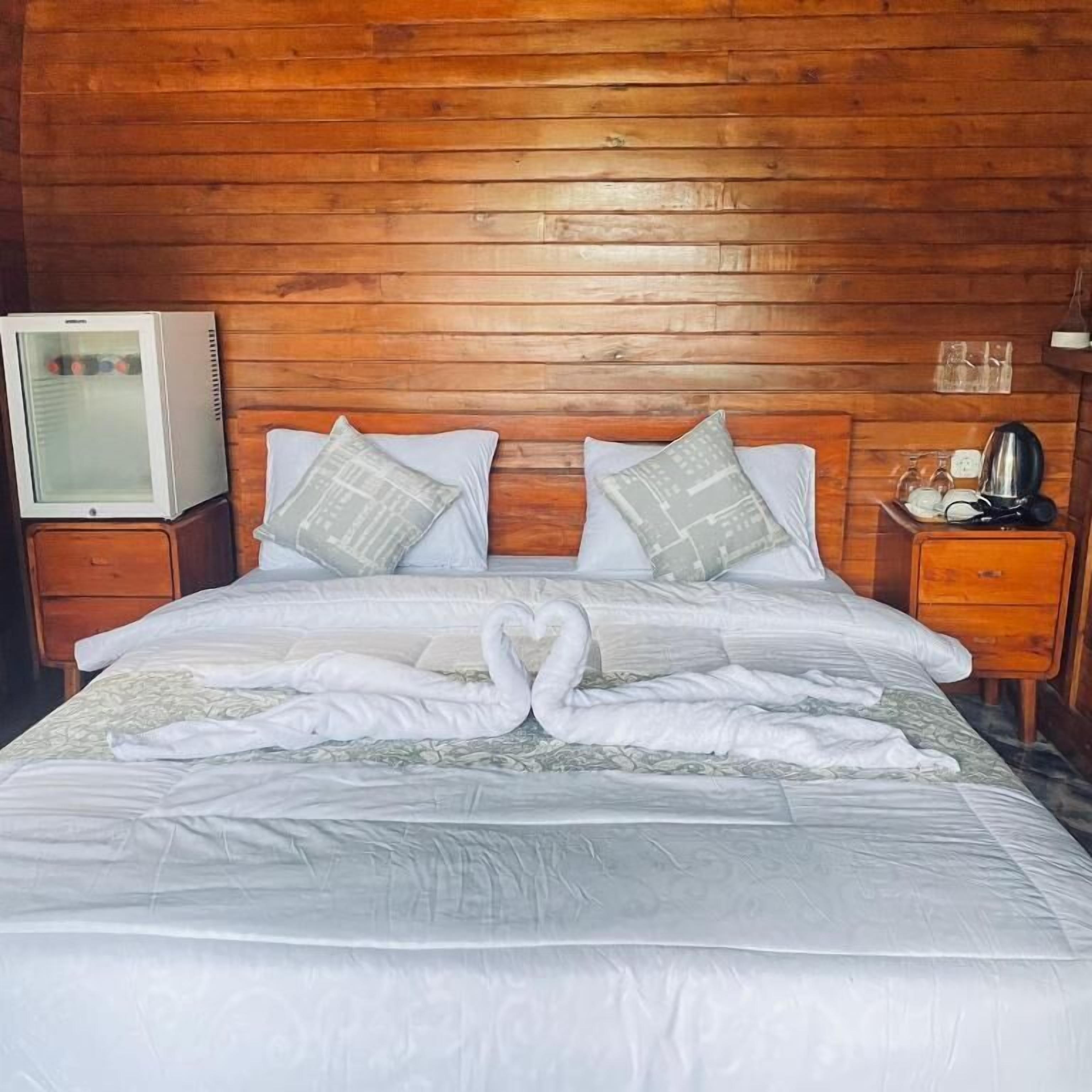 Une chambre d’hôtel avec un plafond en bois, un lit avec une literie blanche, deux oreillers, une table de chevet avec une lampe et un téléviseur posé sur un meuble.