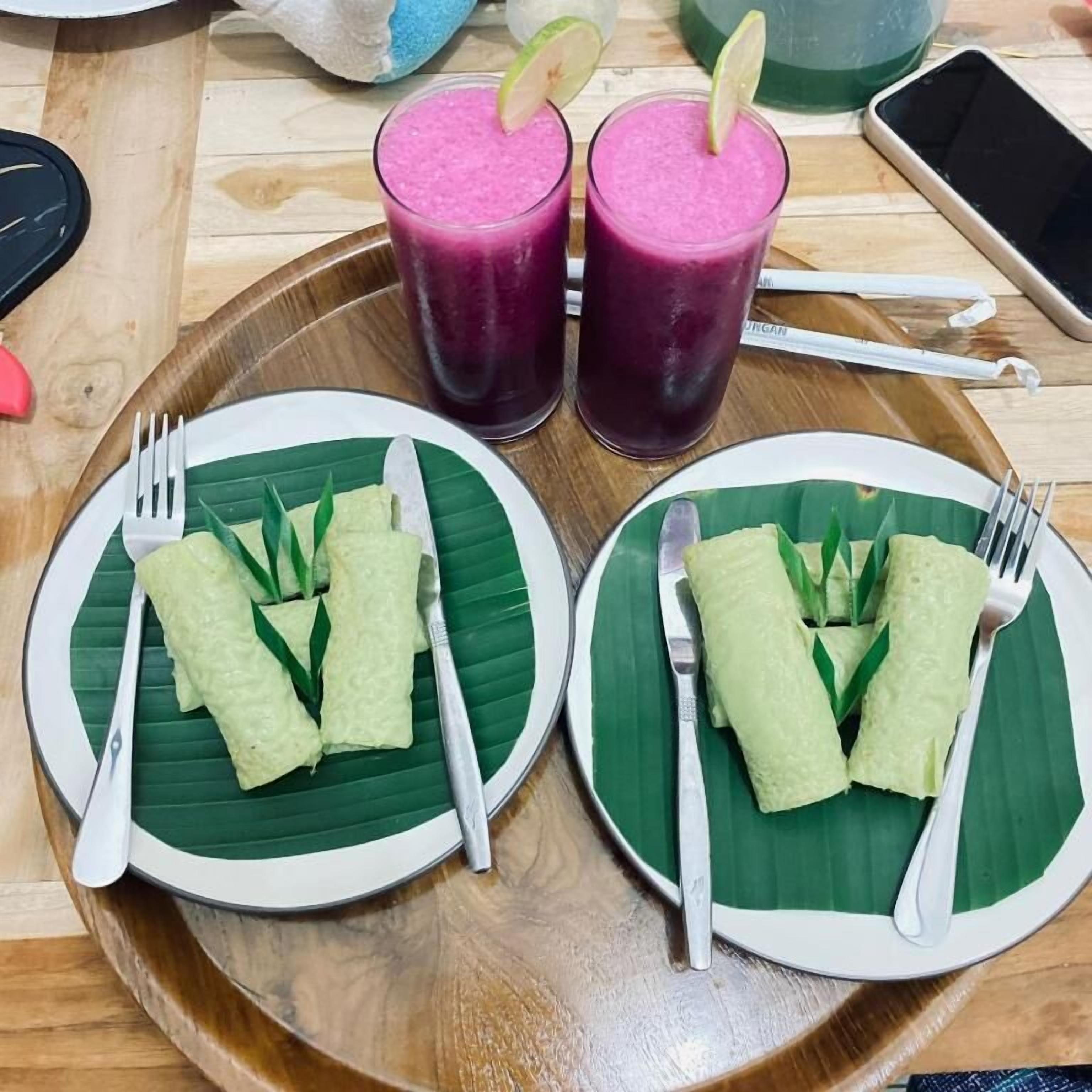 Two plates of food with utensils on a wooden table, accompanied by two drinks.