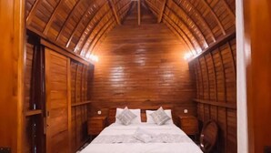 A bedroom with a wooden ceiling, a bed with white bedding, and a patterned floor.