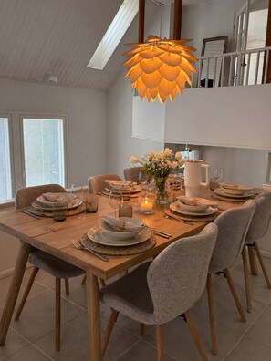 Ein Essbereich mit einem Holztisch, gedeckt für sechs Personen, einer hängenden Pendelleuchte und einer Blumenvase.