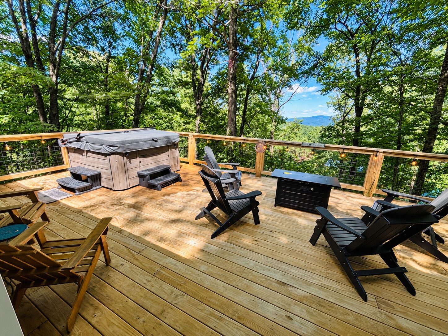 Una terraza de madera con mobiliario exterior, un jacuzzi y vistas a un área boscosa.