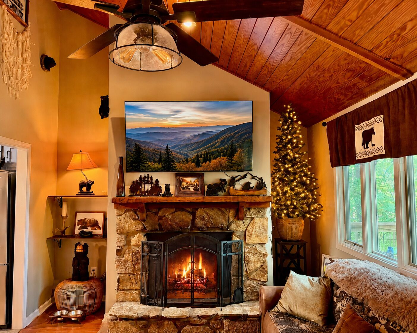 Un salón acogedor con chimenea de piedra, un cuadro grande de un paisaje, un árbol de Navidad y una cortina con temática de osos.