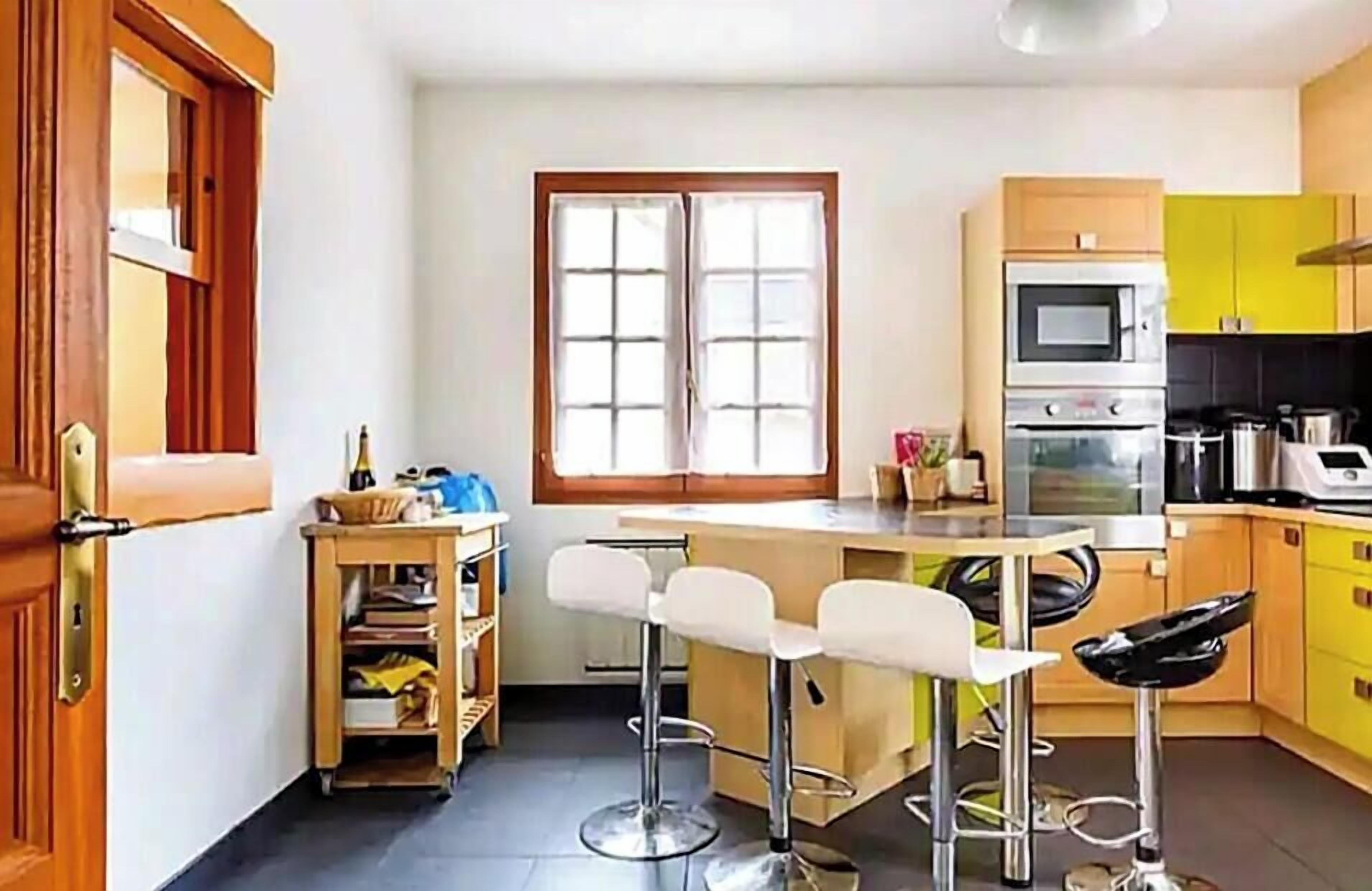 Een kleine keuken met een centraal kookeiland, barstoelen en een raam.