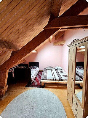 A bedroom with a sloped ceiling, wooden beams, two beds with patterned bedding, a dresser, and a rug.