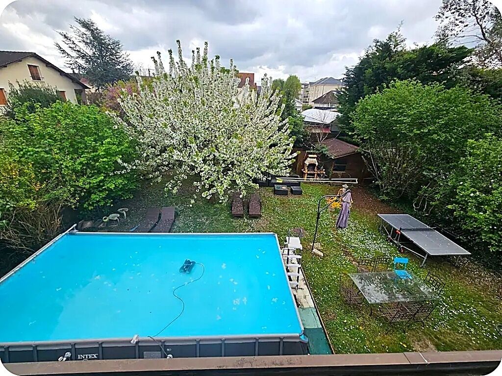 En swimmingpool med en omgivande terrass, en uteplats med ett bord och stolar samt en trädgård med blommande träd.