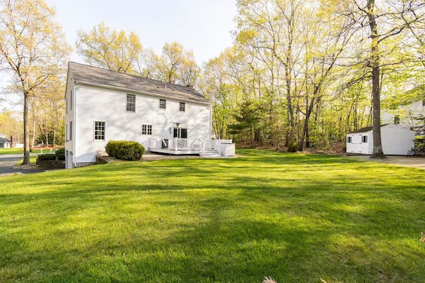 A white two-story house with a front porch, surrounded by a well-maintained lawn and trees.
