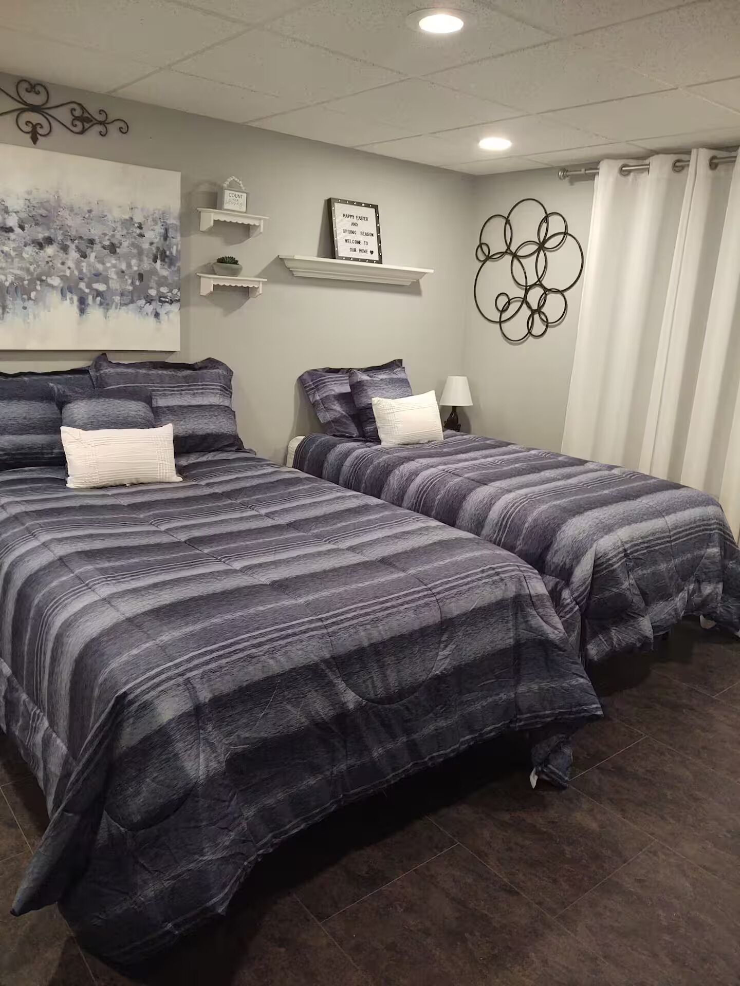A bedroom with two beds, a painting, a sign, and a decorative wall piece.
