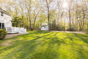 A residential property with a well-maintained lawn, a white house with a porch, and a small shed in a wooded area.