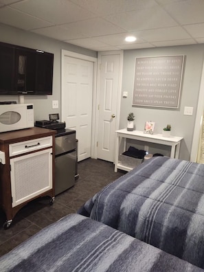 A hotel room with a bed, a desk with a computer, a microwave, a refrigerator, and a television.