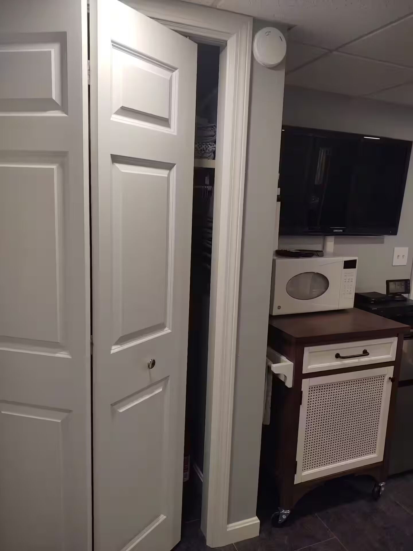 Una stanza con una porta chiusa, una televisione, un forno a microonde e un piccolo armadietto.