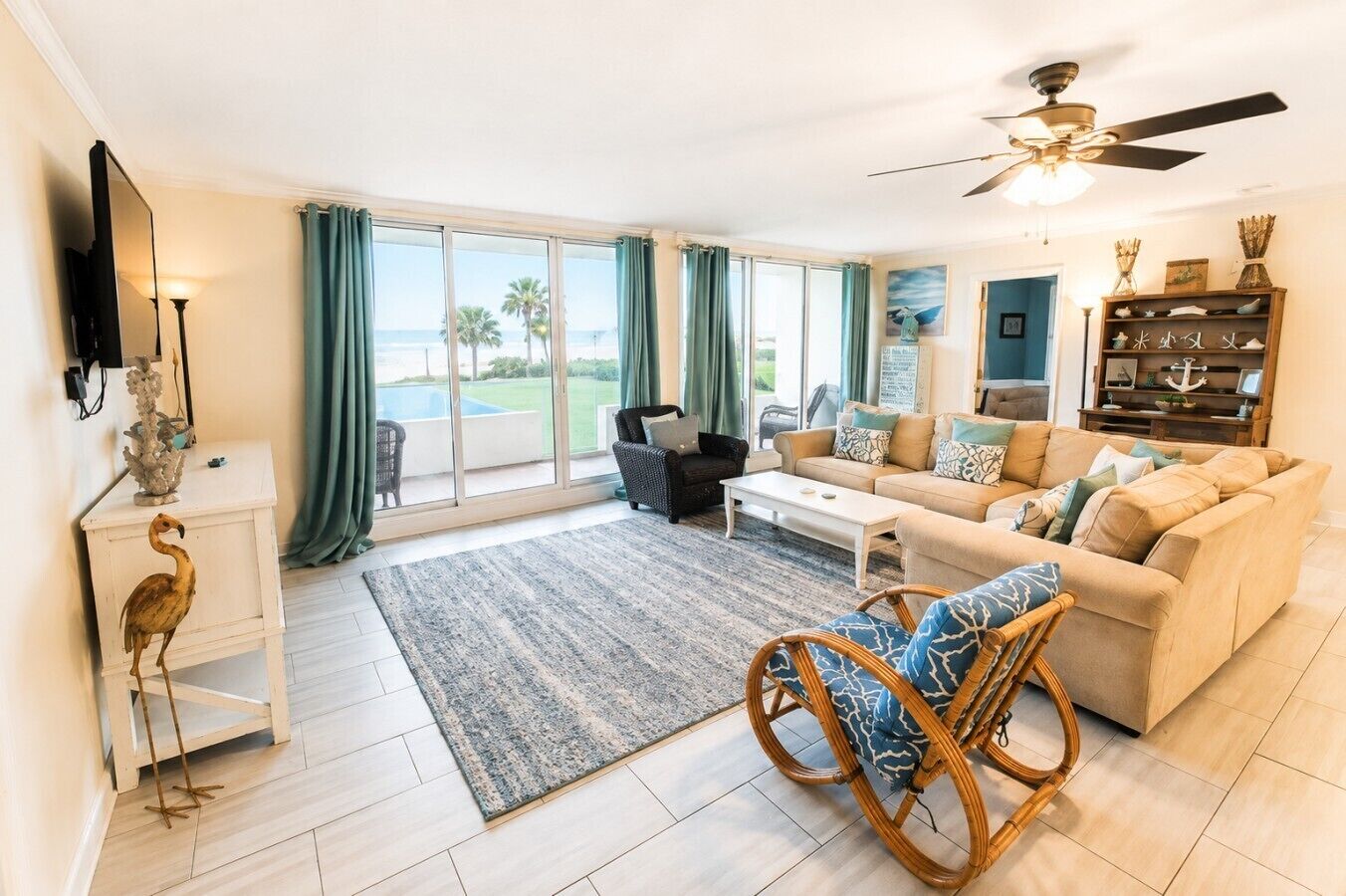A spacious living room with a large window, a ceiling fan, and a view of the ocean.