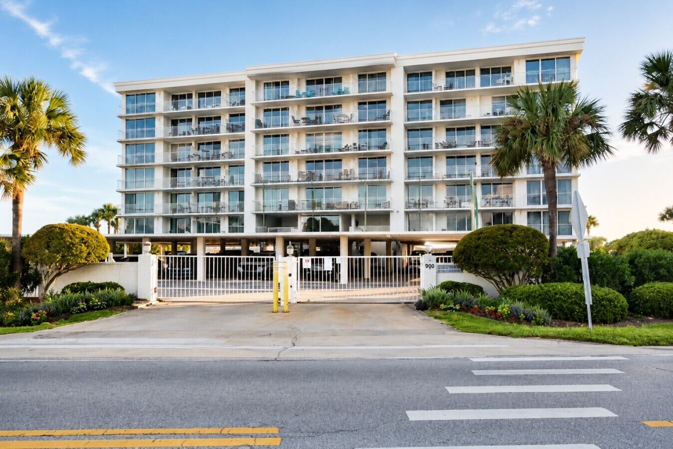 A multi-story hotel with a gated entrance, palm trees, and a clear sky.