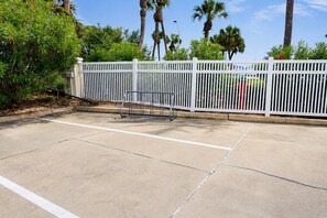 Ein gepflasterter Parkplatz mit weißen Metallschranken und einem weißen Zaun.