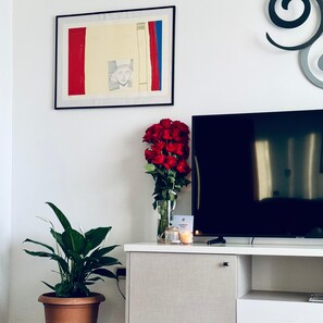 A room with a television, a framed abstract artwork, a vase with red roses, and a potted plant.