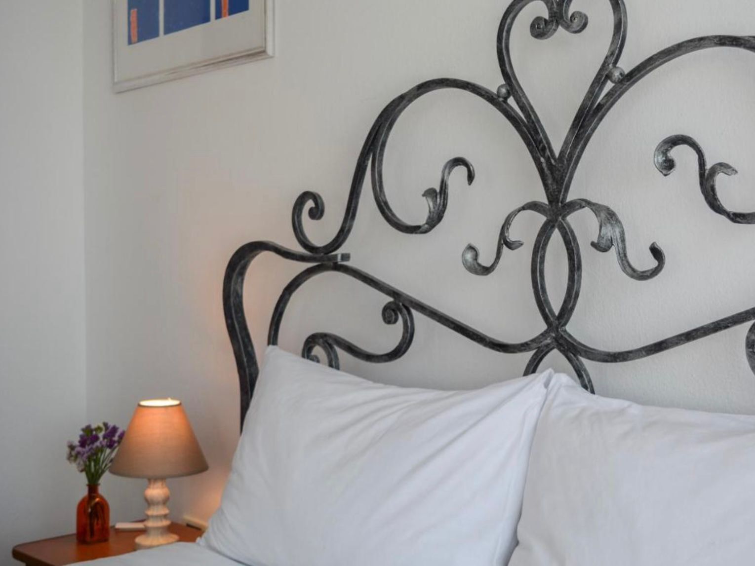 A bed with a metal headboard, a bedside table with a lamp, and a framed picture on the wall.