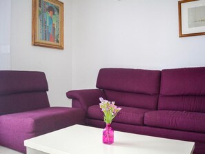Een woonkamer met een paarse bank, een witte salontafel en een vaas met bloemen.