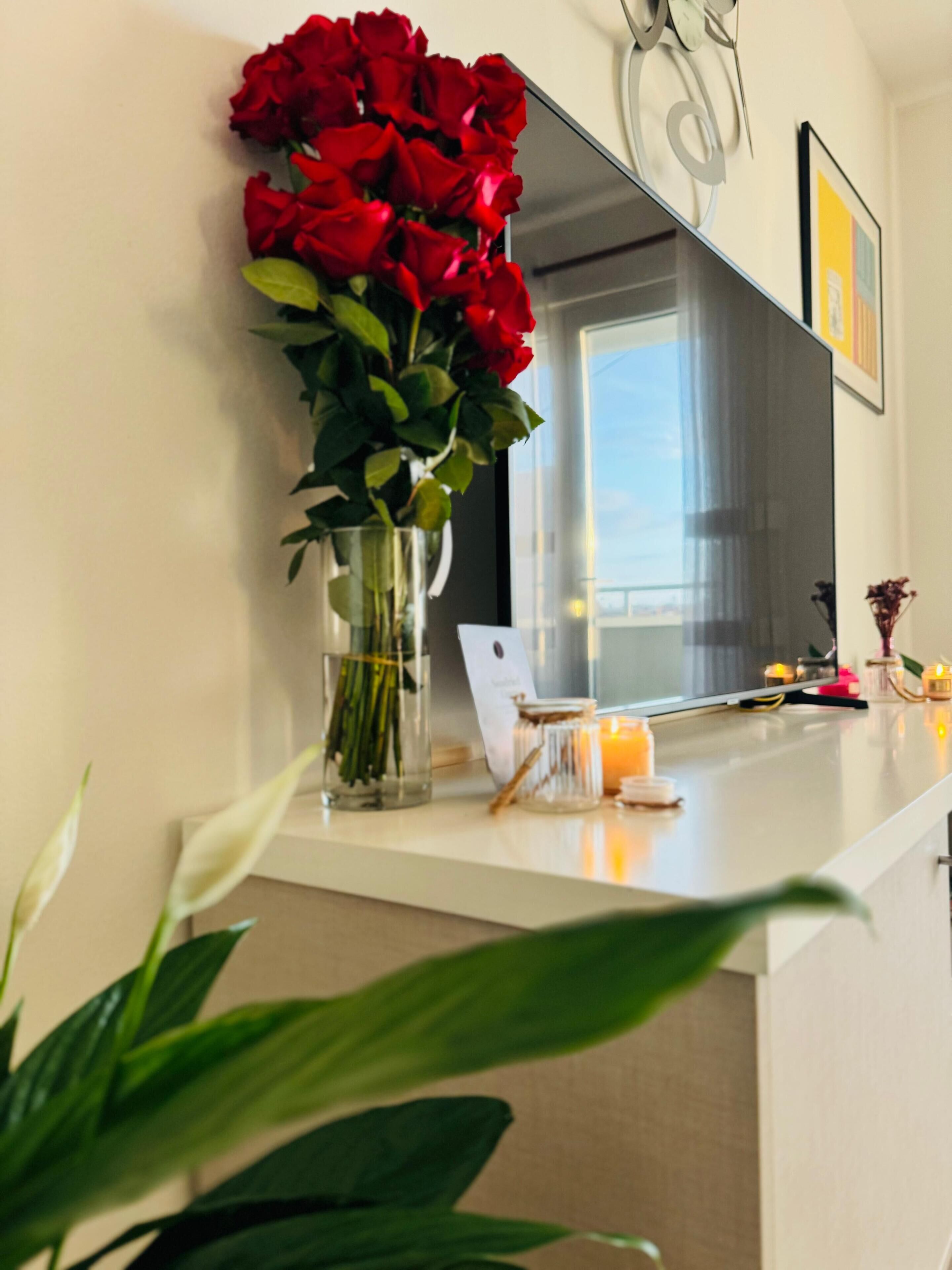 Un comptoir de cuisine orné d’un vase de roses rouges, d’une bougie et d’un tableau encadré accroché au mur.