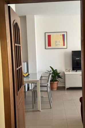 Een moderne woonkamer met een eethoek, een flatscreen televisie, een potplant en een kunstwerk in een lijst aan de muur.