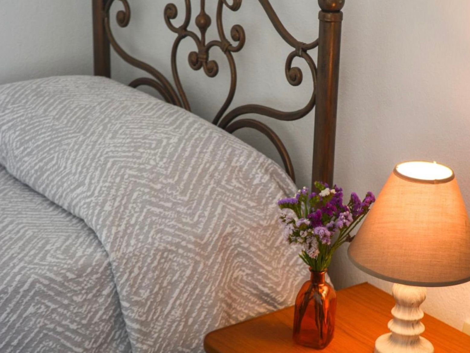 Een bed met een gebloemd deken, een vaas met bloemen en een tafellamp.