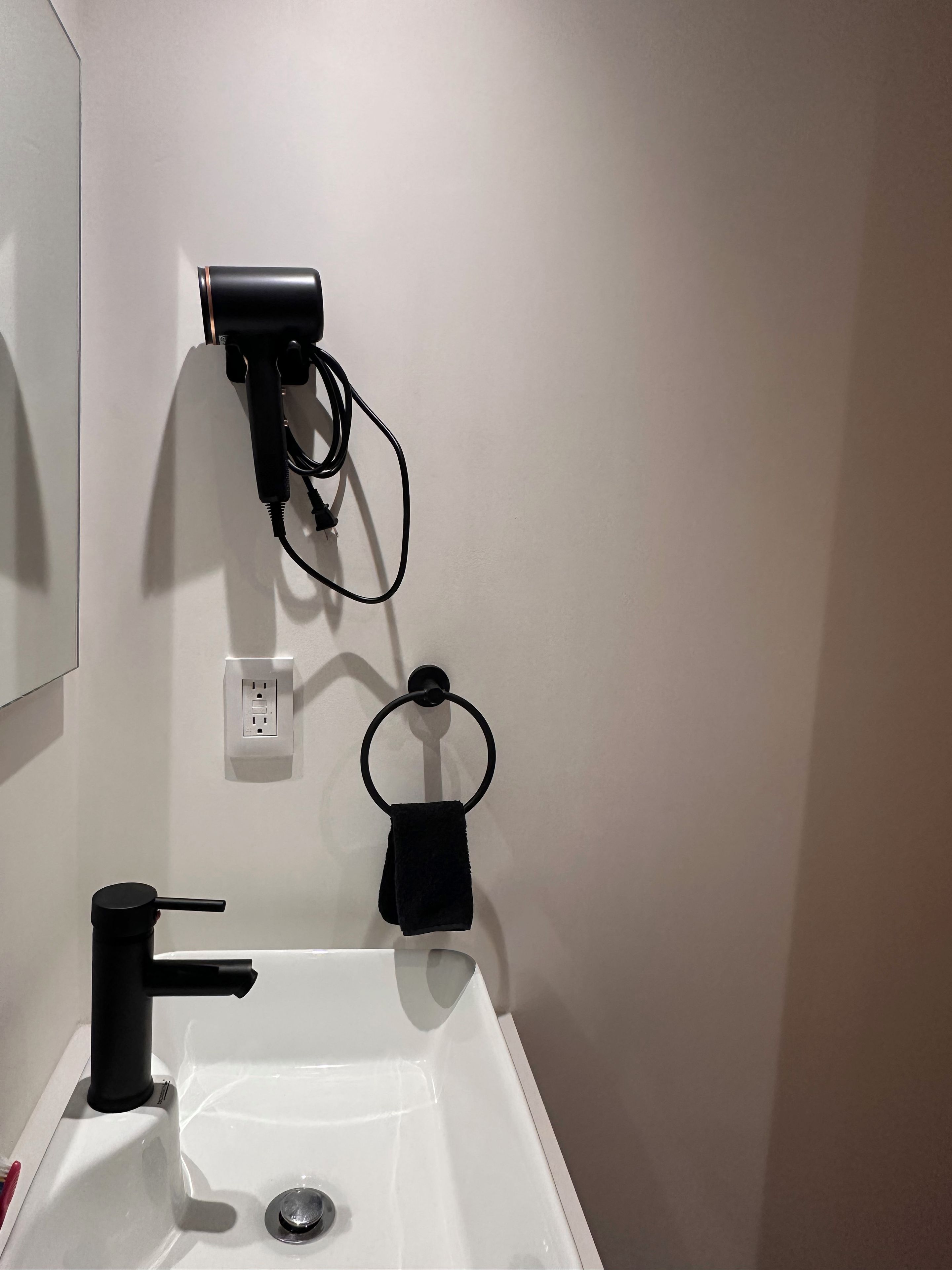 A bathroom with a white sink, a black faucet, a hairdryer mounted on the wall, and a towel ring.
