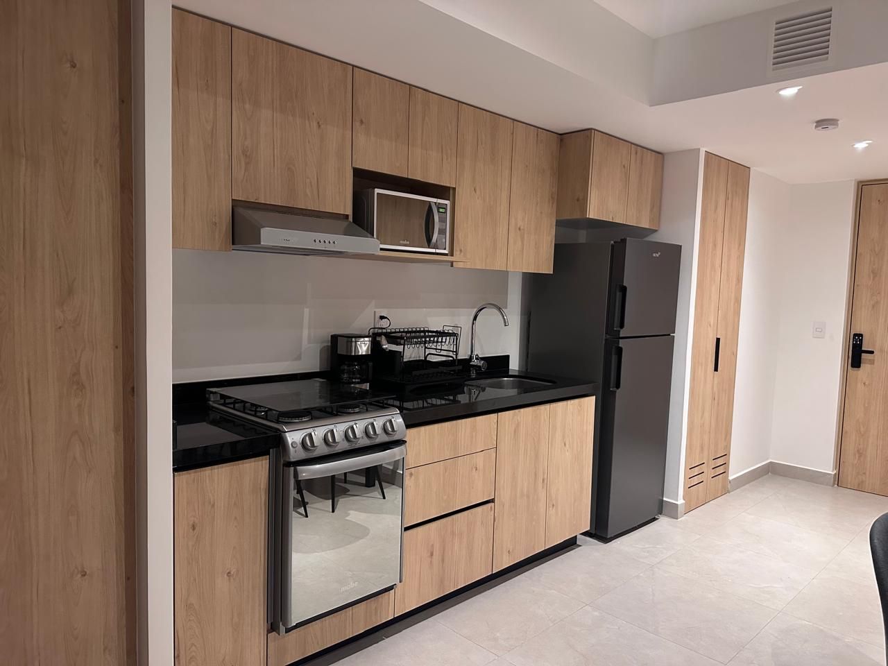 Une cuisine moderne avec des meubles en bois, un réfrigérateur en acier inoxydable, un four à micro-ondes encastré et une cuisinière à gaz.