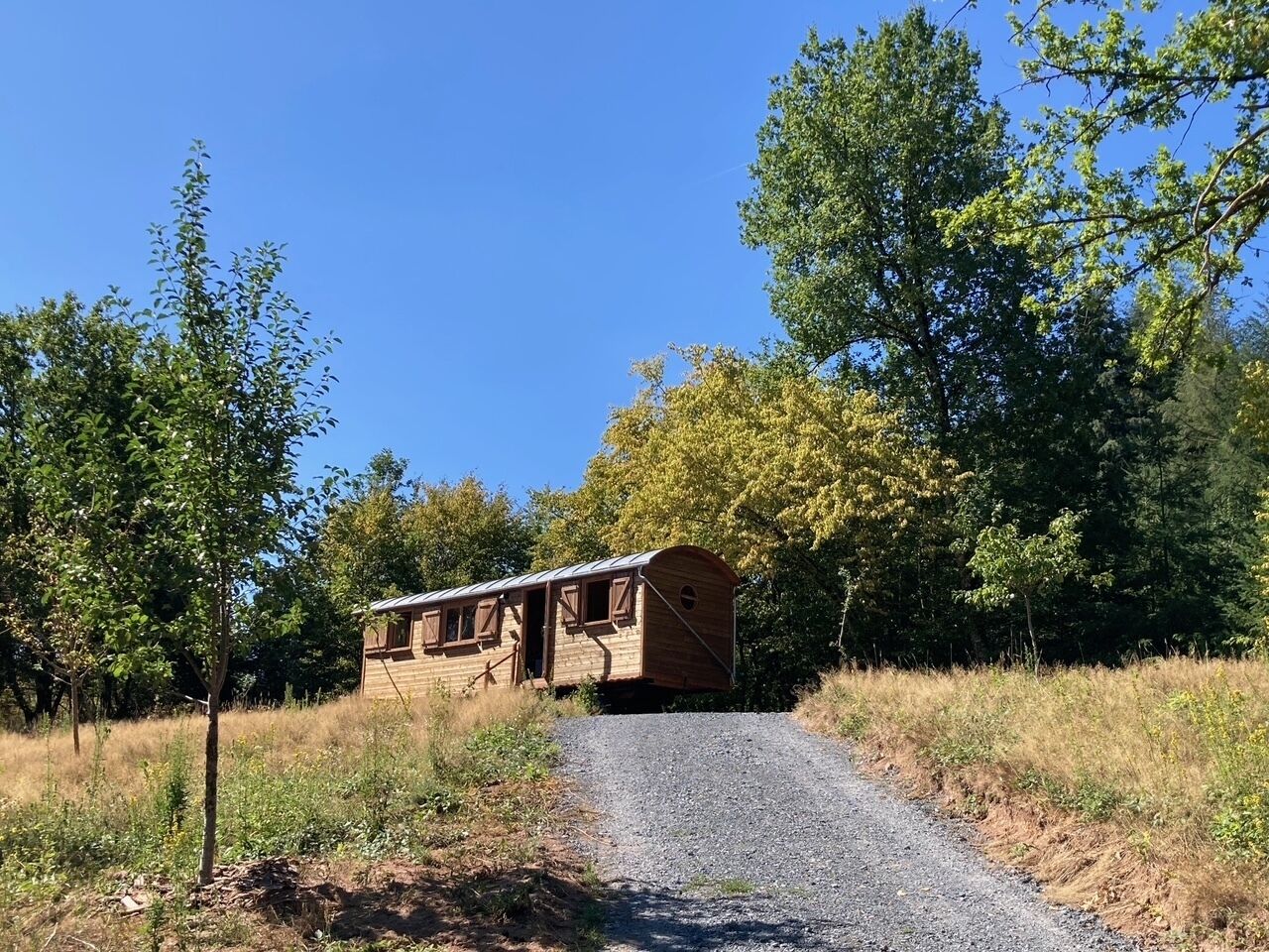 A wooden structure with a sloped roof, situated on a gravel path surrounded by trees.