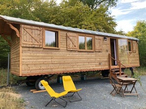 A wooden house with a metal roof, a sliding door, and a small porch area. - Morvan-style caravan (Dun-les-Places)