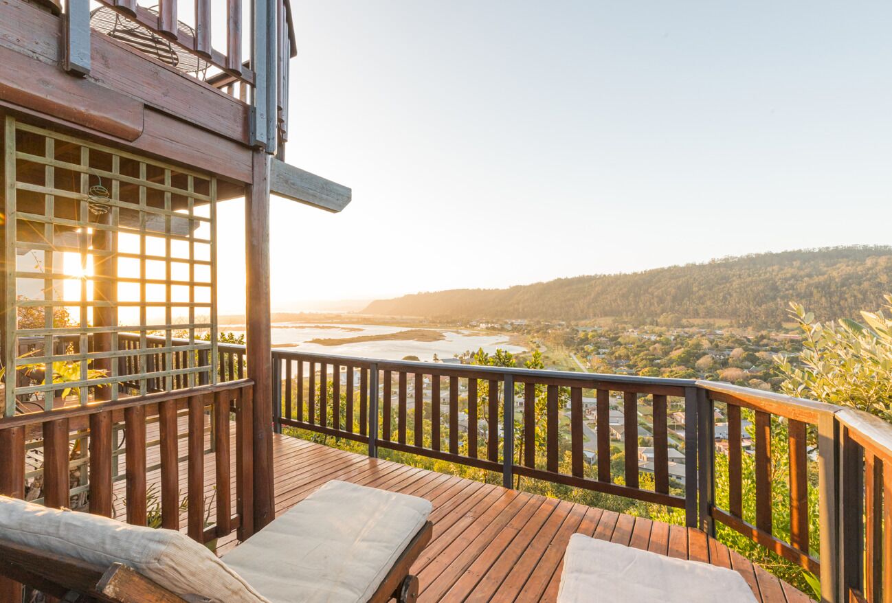 A wooden deck with two lounge chairs, overlooking a river and a forested landscape.